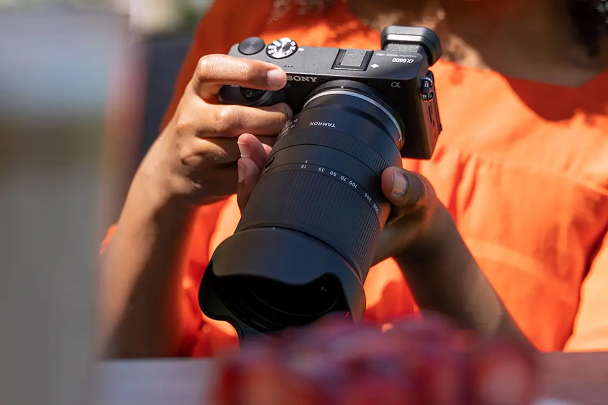 Hands holding a Sony camera with Tamron 18-300mm lens during an outdoor family photography session.