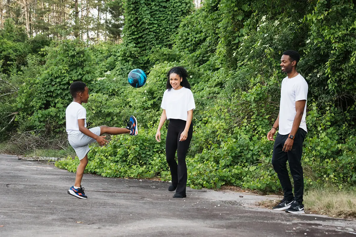 Family playing soccer together outdoors during a candid family photography session.