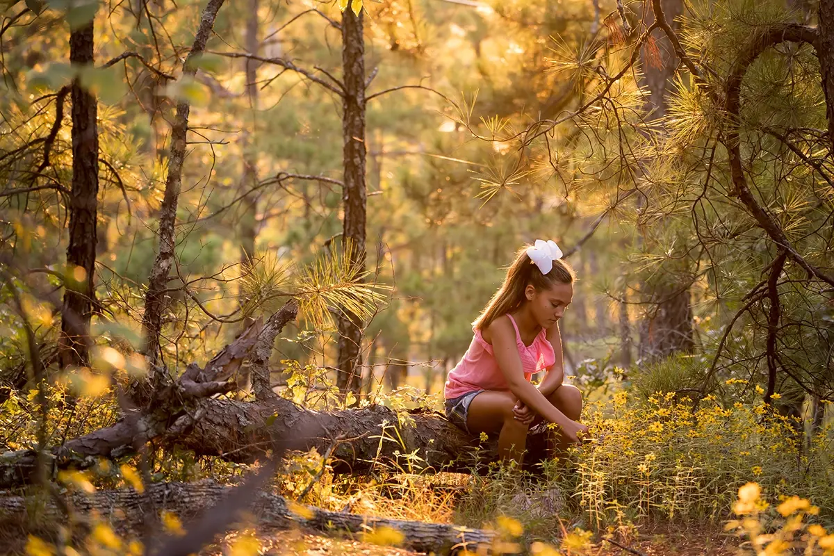 Fotografía de la hora dorada retrato a contraluz de niña en el bosque.