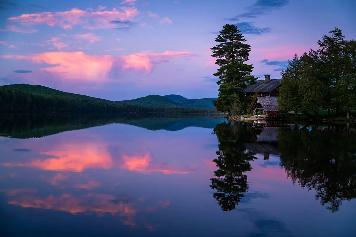 Fotografía en hora azul de reflejos de lago con montañas y cabaña.