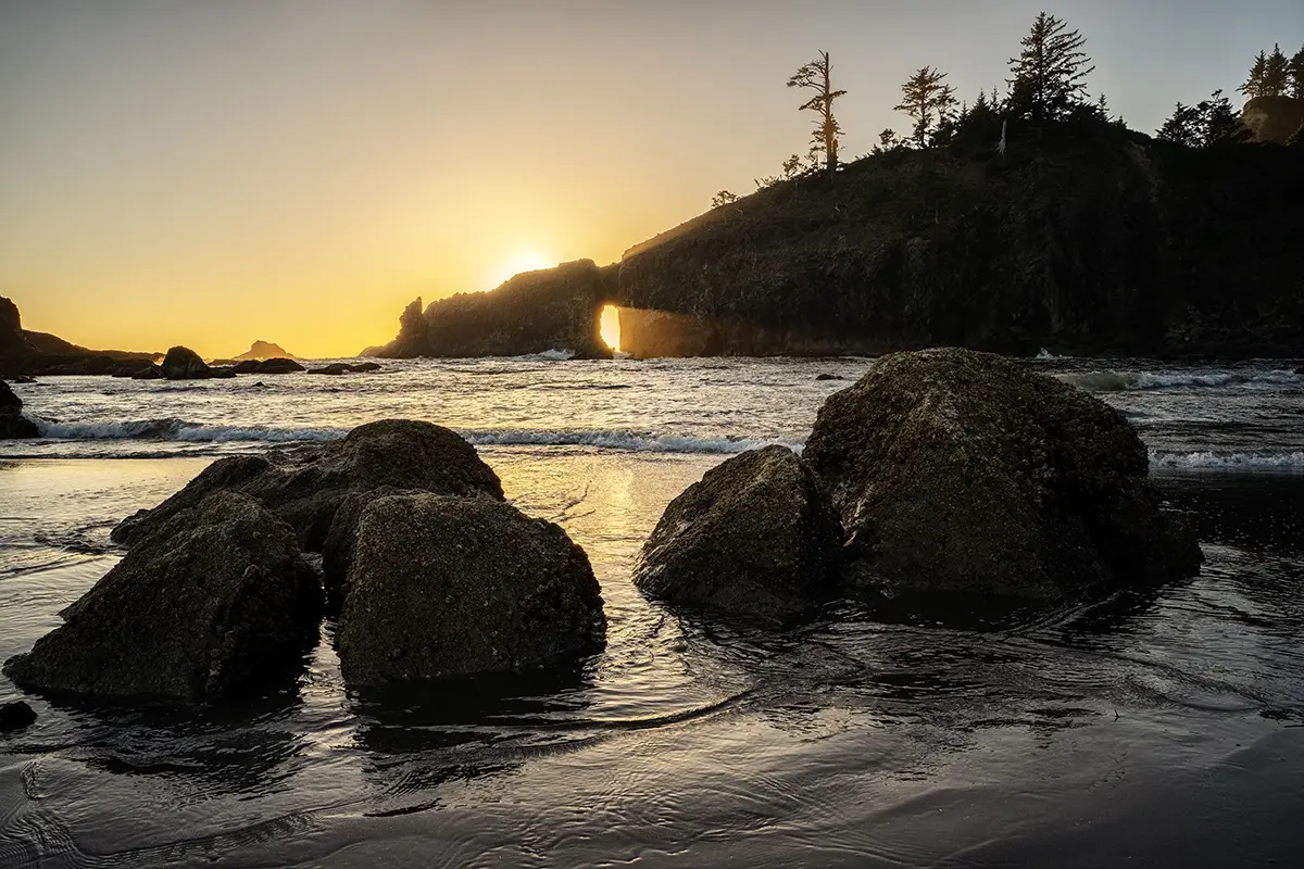 Puesta de sol en hora dorada sobre playa rocosa con acantilados marinos.