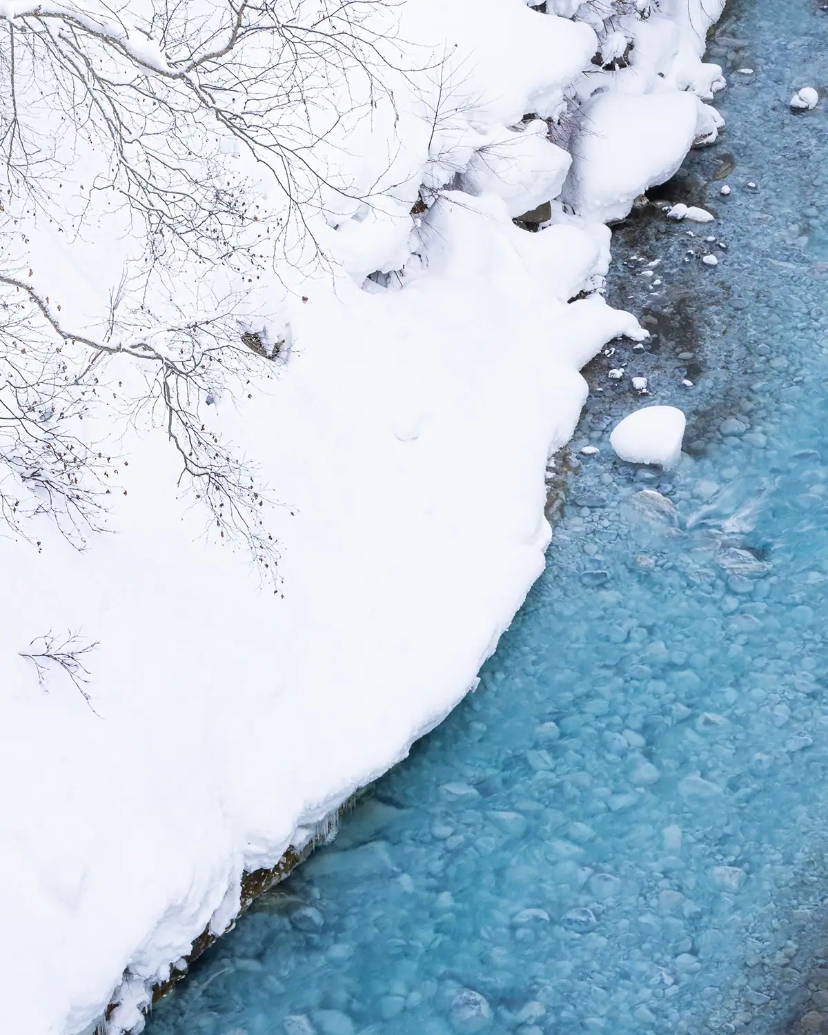 Orilla del río cubierta de nieve y agua azul helada en Hokkaido durante el invierno