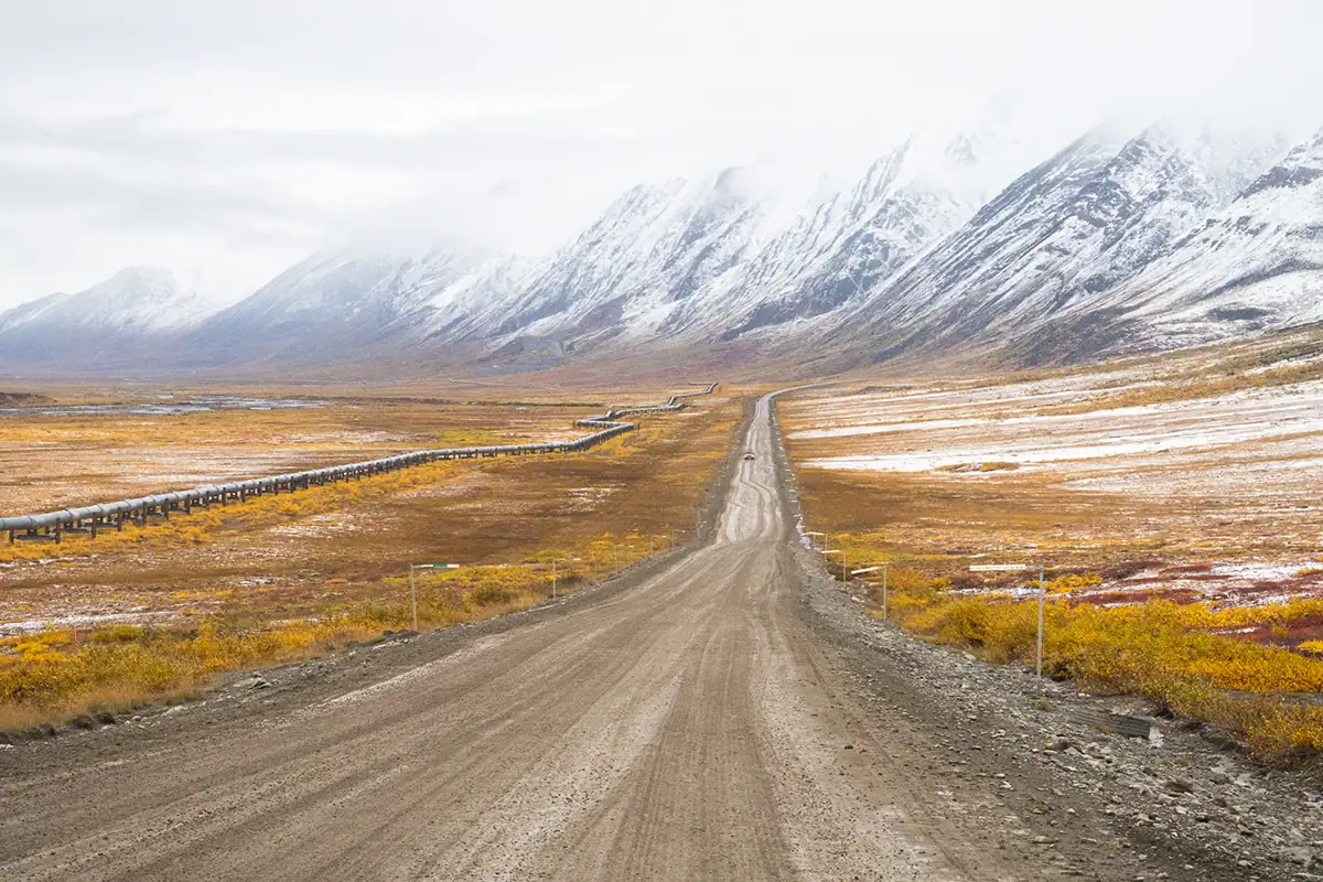 Dalton Highway leading toward snow-covered Brooks Range during Alaska fall colors&mdash;an iconic scene of landscape photography Alaska in autumn.