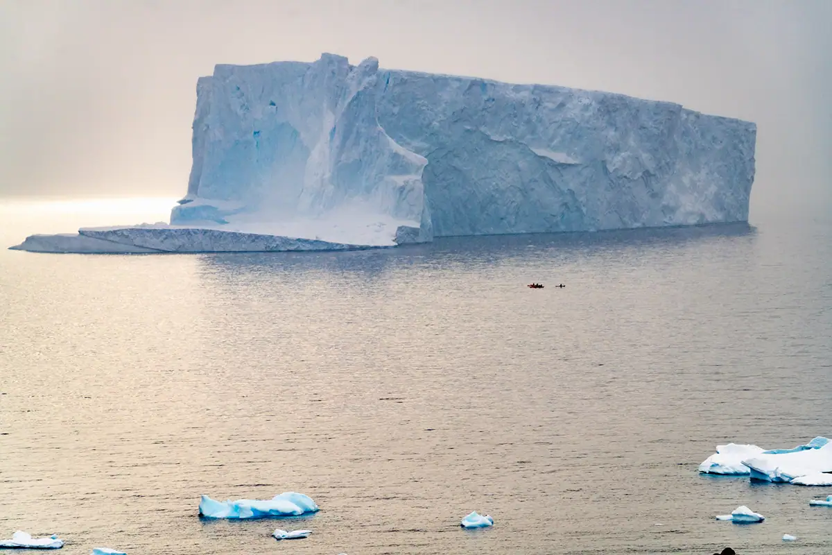 Kayakers paddling near a massive iceberg during an Antarctica cruise photography expedition.