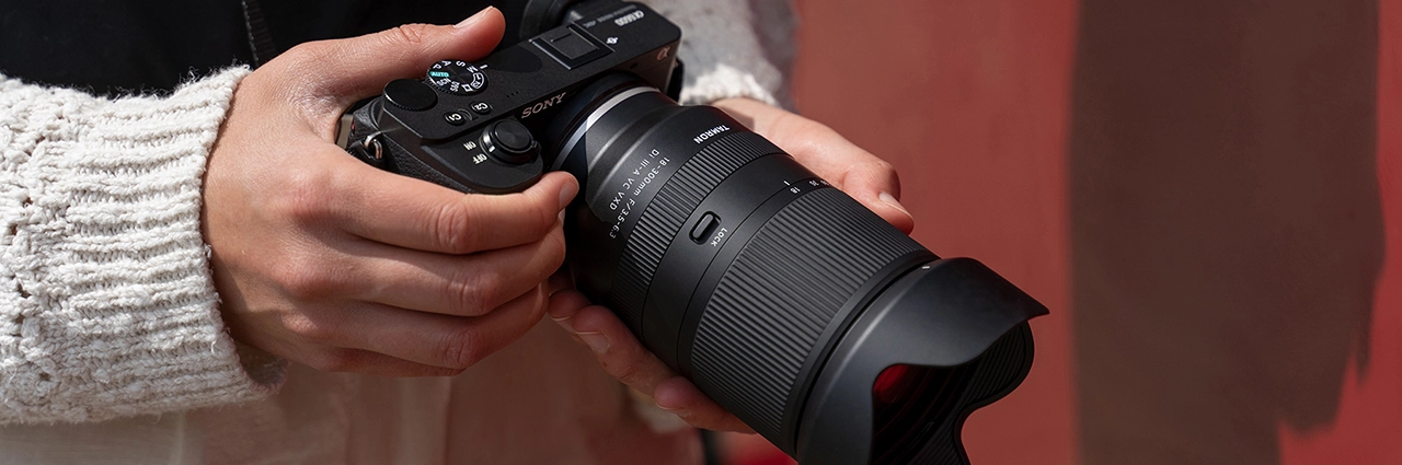 Person holding a Sony APS-C mirrorless camera with Tamron 18-300mm F3.5-6.3 lens.