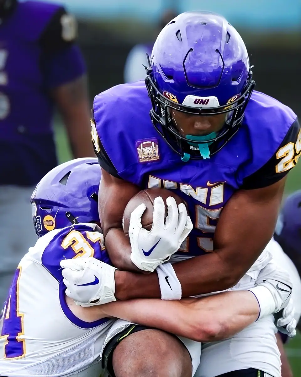 Un joueur de football qui porte le ballon et se fait plaquer.