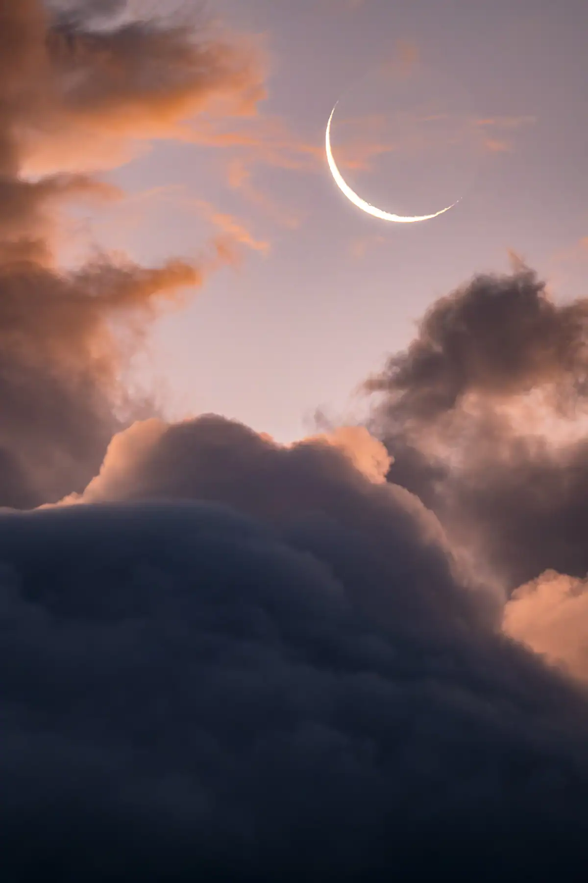 Crescent moon photographed at dusk above colorful clouds.