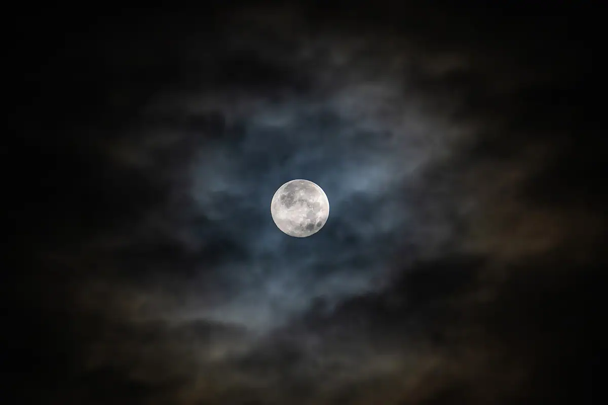 Full moon shining through clouds in a night sky, creating a hazy effect.