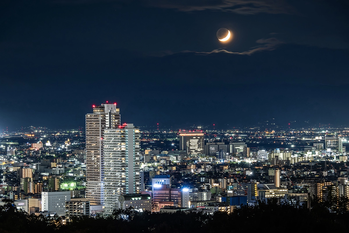 Crescent moon photographed above a city skyline at night.
