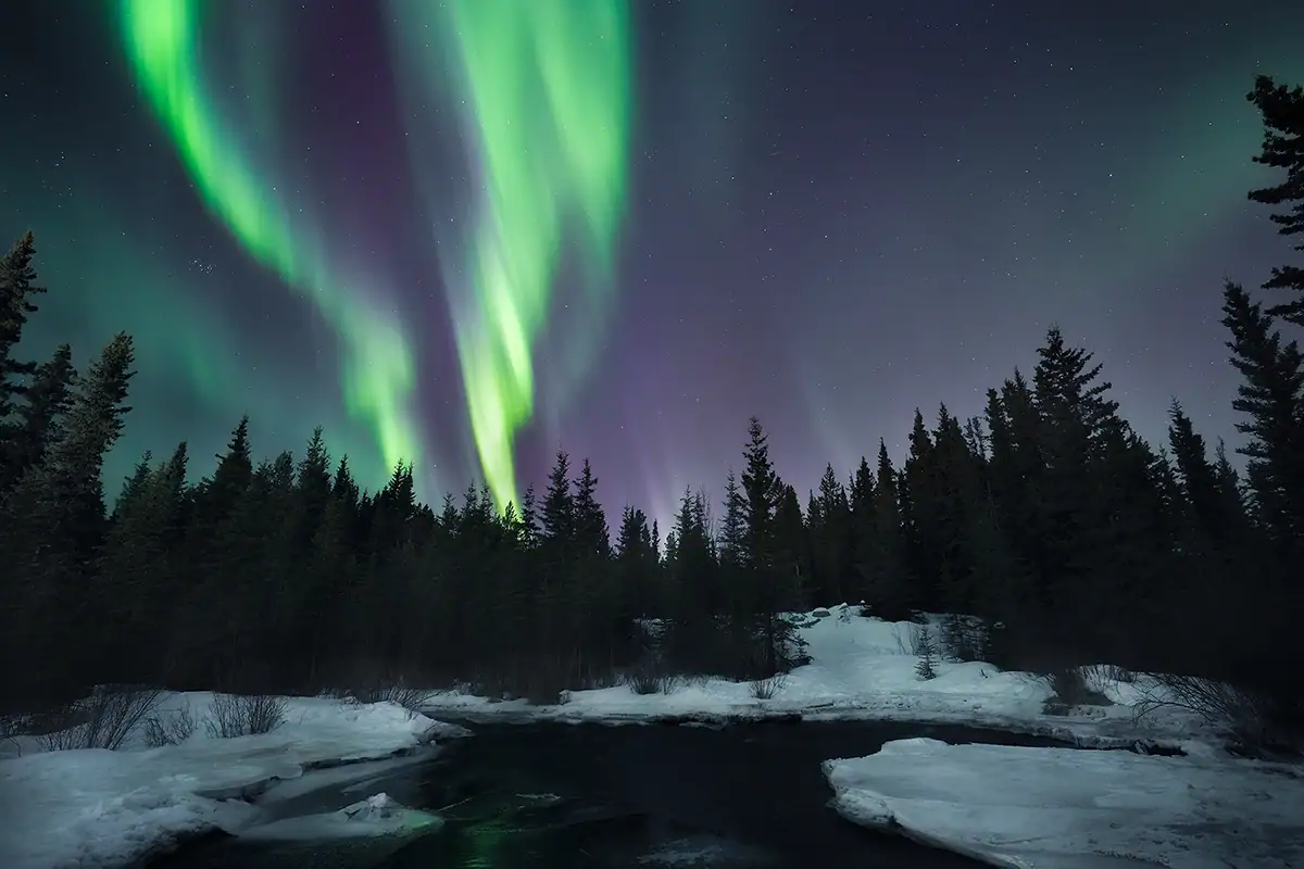 Mesmerizing Northern Lights illuminate the night sky above Bruarfoss waterfall in Iceland, with smooth flowing water and snow-covered terrain.