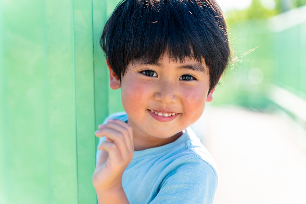 Portrait of a smiling child with a simple blurred background, showing less background information in composition.