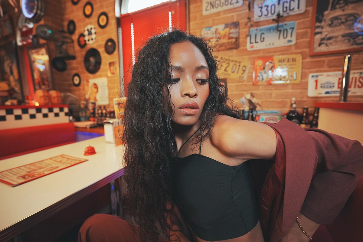 Portrait of a woman in a retro diner with detailed background elements, showing more background information in composition.