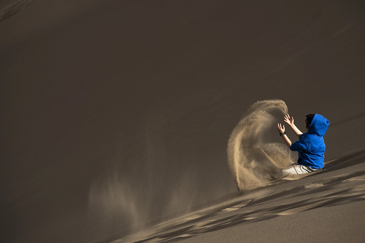 Person in a bright blue hoodie playing with sand on a dune, creating strong color and texture contrast for contrast composition.