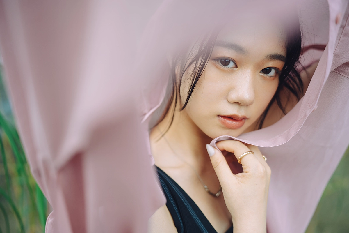 Portrait of a woman framed by soft pink fabric in the foreground, showing layering in photography.