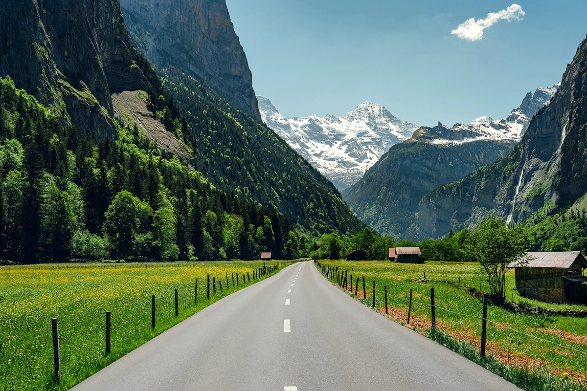 Straight road leading through green fields toward snow-capped mountains, demonstrating leading lines in photography.
