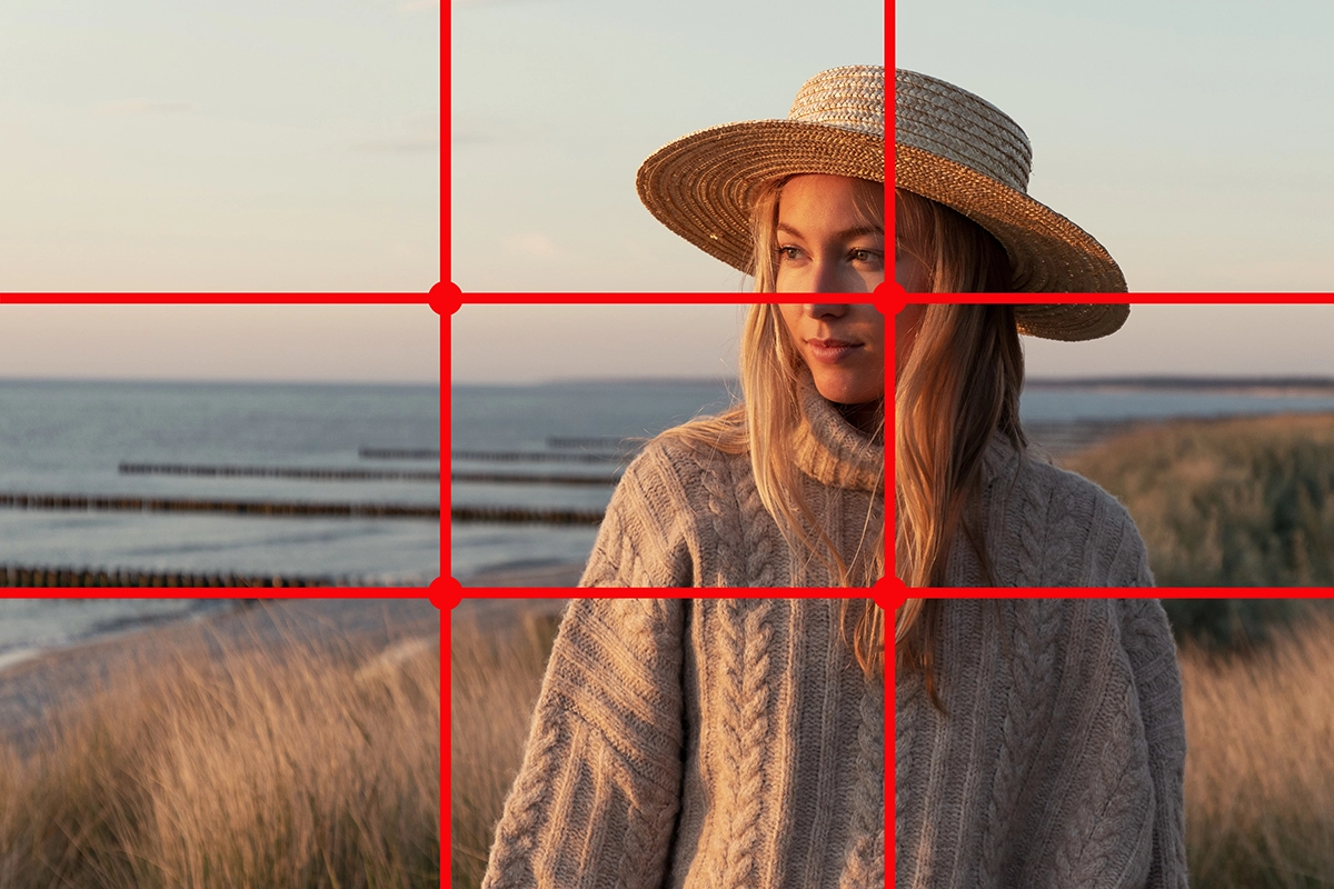 Portrait of a woman on the beach wearing a hat, with a red rule of thirds grid overlay demonstrating composition.