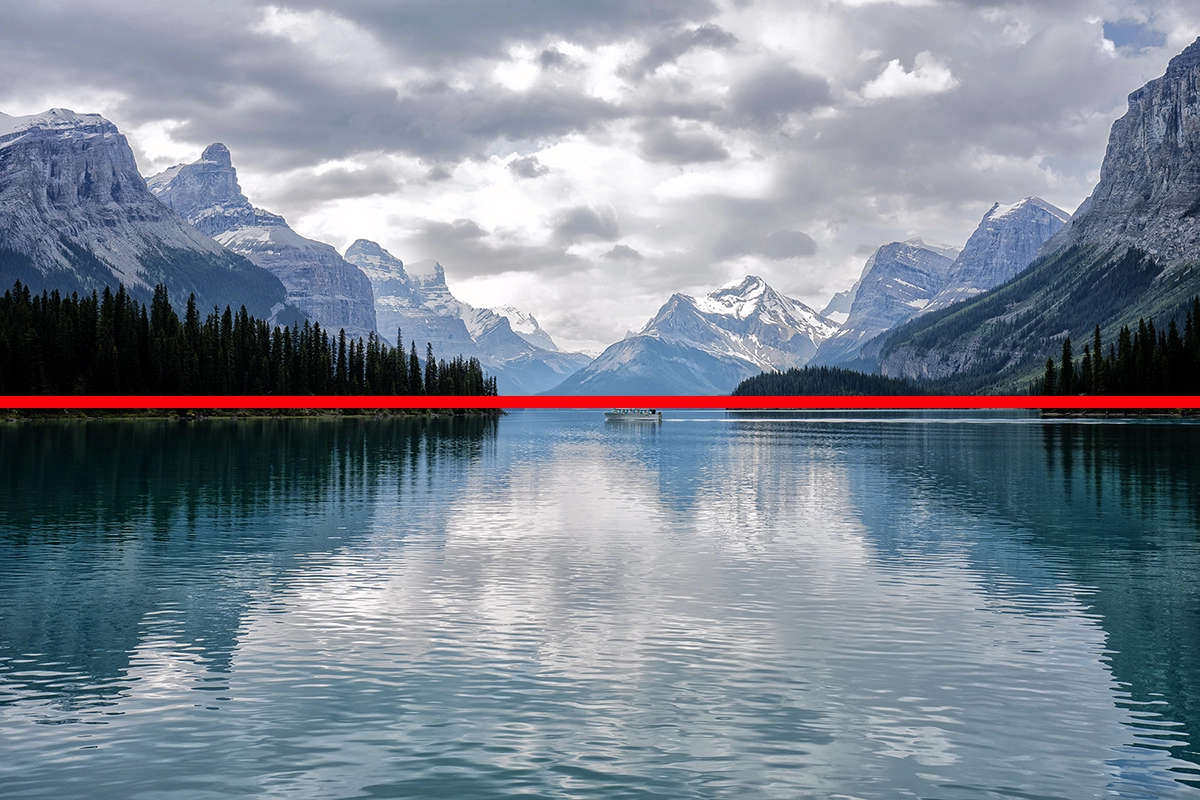 Mountain lake with reflections of peaks and trees, divided by a red horizontal line to demonstrate symmetry composition.