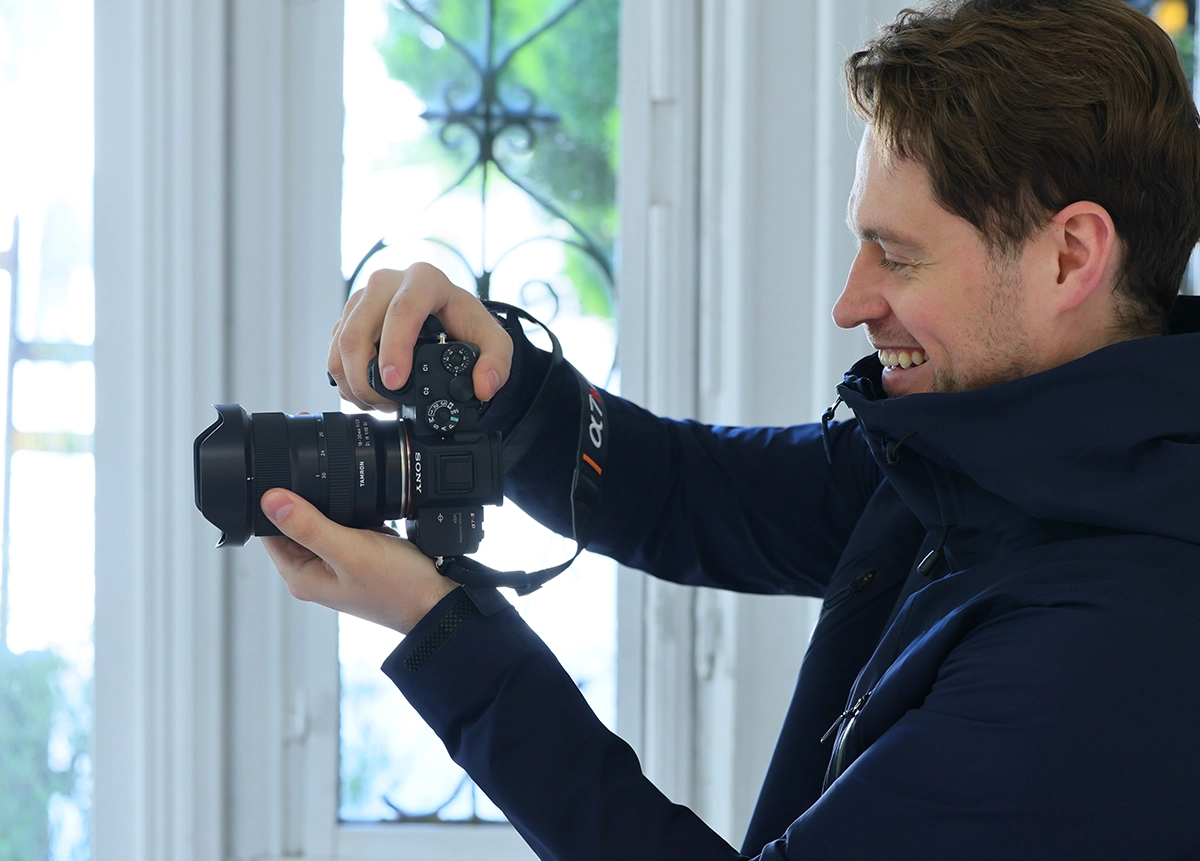 Smiling man holding a Sony camera with a Tamron lens, demonstrating use of equipment for beginner photography composition.