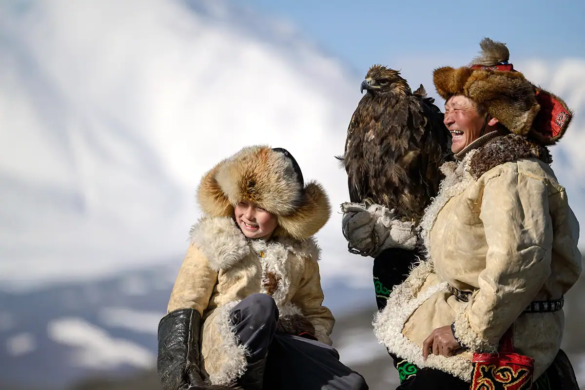 Dos personas vestidas con ropa tradicional de piel con un águila real, capturadas en formato de imagen RAW para conservar la textura, el detalle y el rango dinámico.