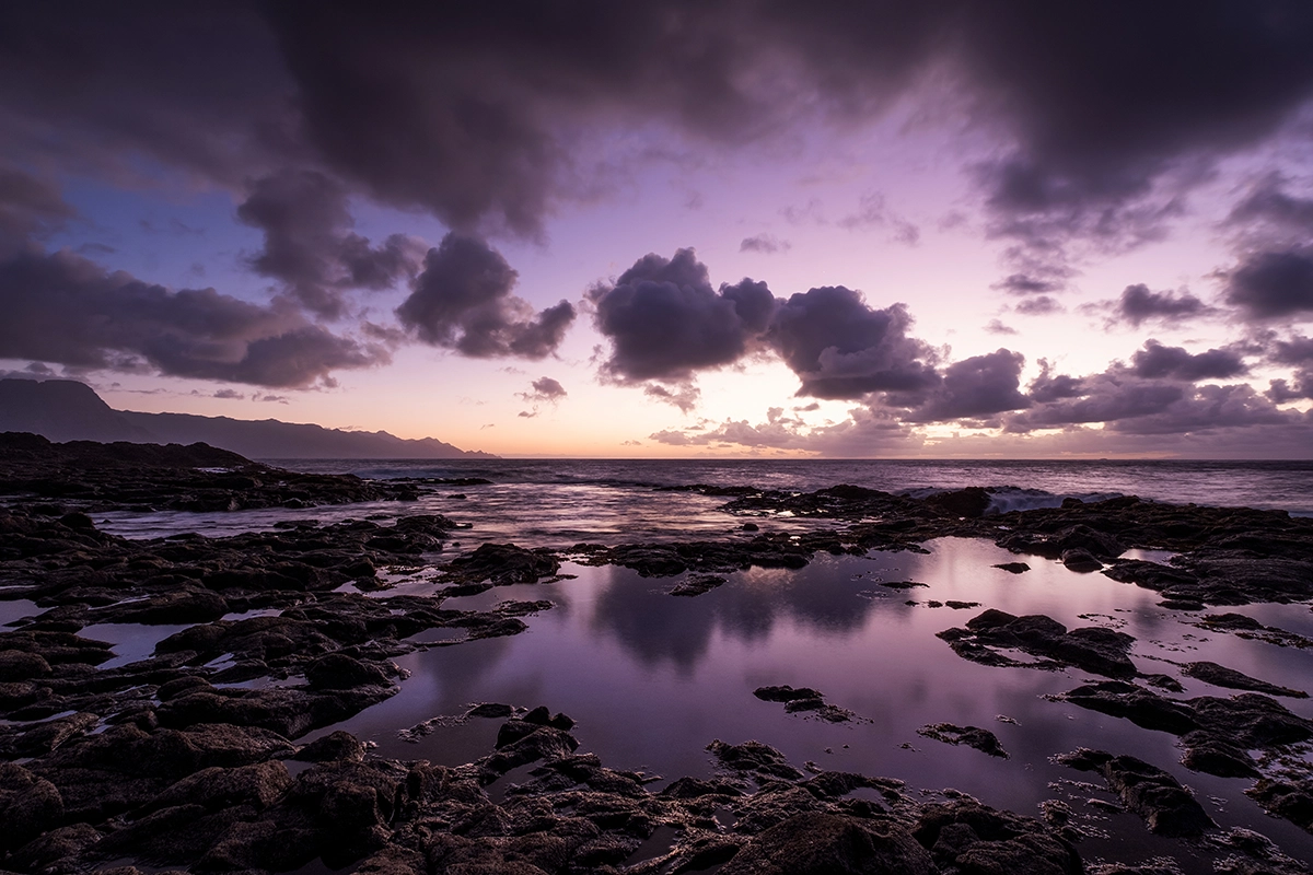 Dramatic purple sunset over lava rock formation and water shot with Tamron wide-angle lens for Fujifilm X cameras.