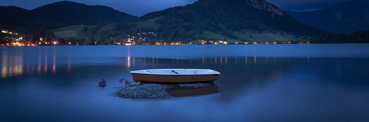 Small boat resting on a calm lake during blue hour with mountains in the background.