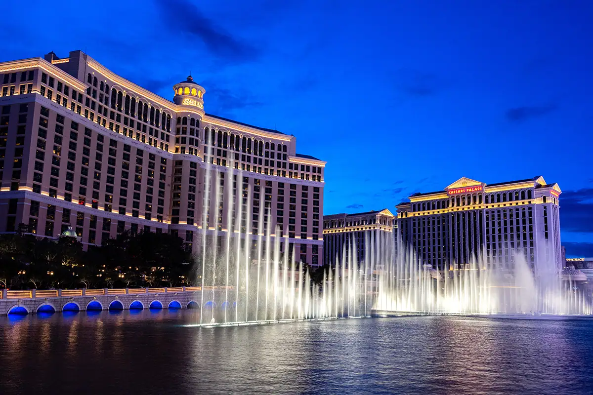 Illuminated fountains in front of Las Vegas hotels during blue hour.