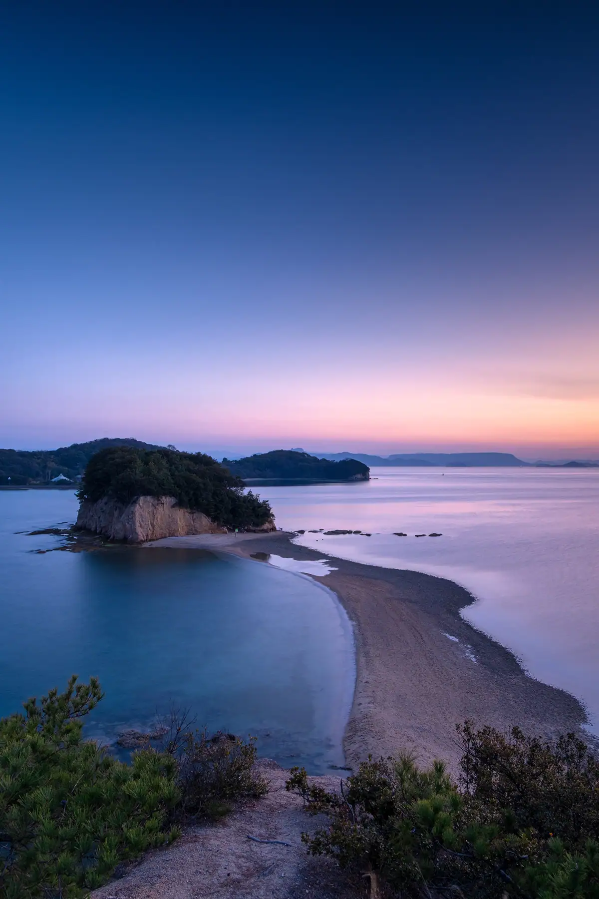 Small island and shoreline at blue hour with calm ocean.