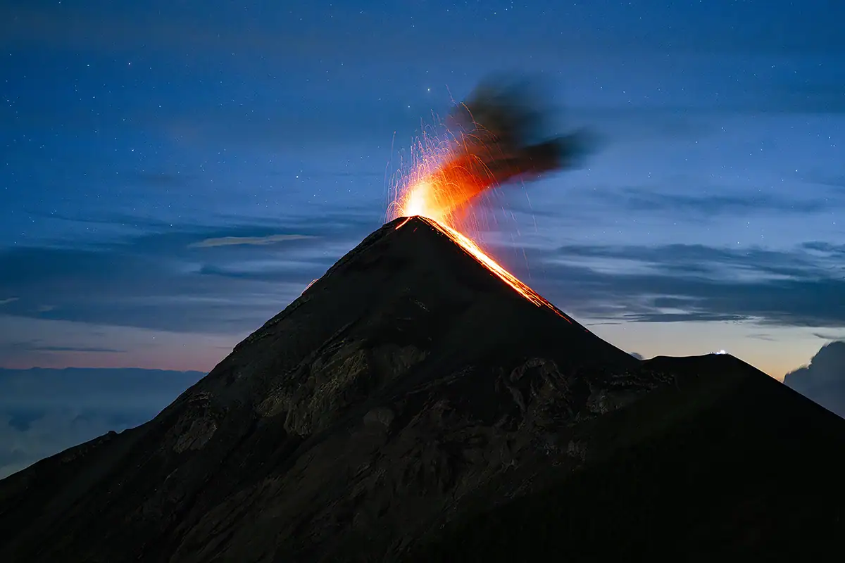 Volcano erupting with lava and smoke during blue hour.