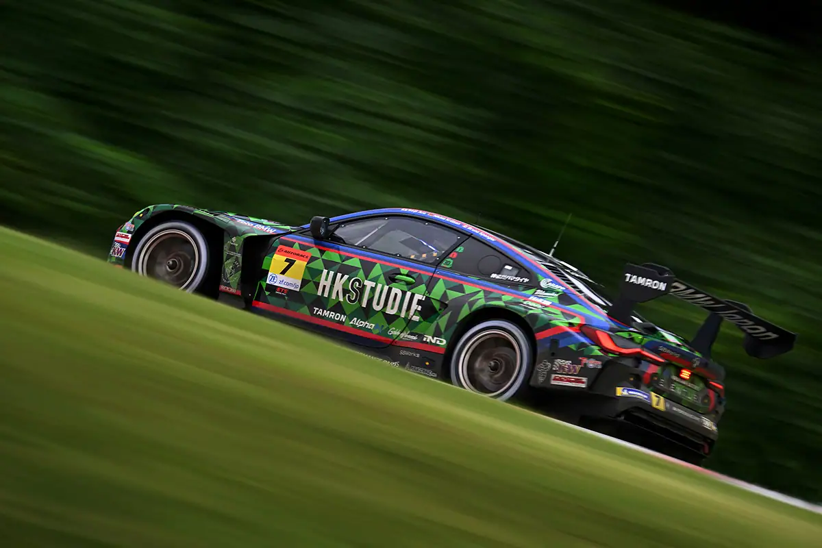 Colorido coche de carreras circulando a toda velocidad por una pista, capturado con una técnica de panorámica, que muestra detalles nítidos del vehículo sobre un fondo verde difuminado por el movimiento.