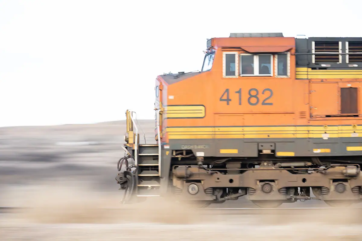 Tren de mercancías naranja en movimiento capturado con una técnica de barrido, que muestra un tren nítido sobre un fondo borroso para transmitir velocidad.