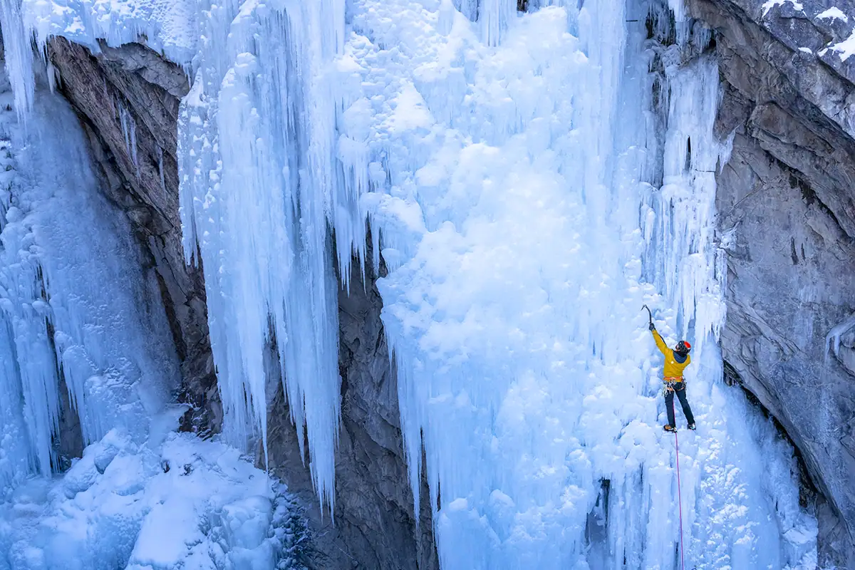 Un grimpeur de glace vêtu de jaune escalade un mur de glace bleue scintillante dans le célèbre Ice Park d'Ouray.