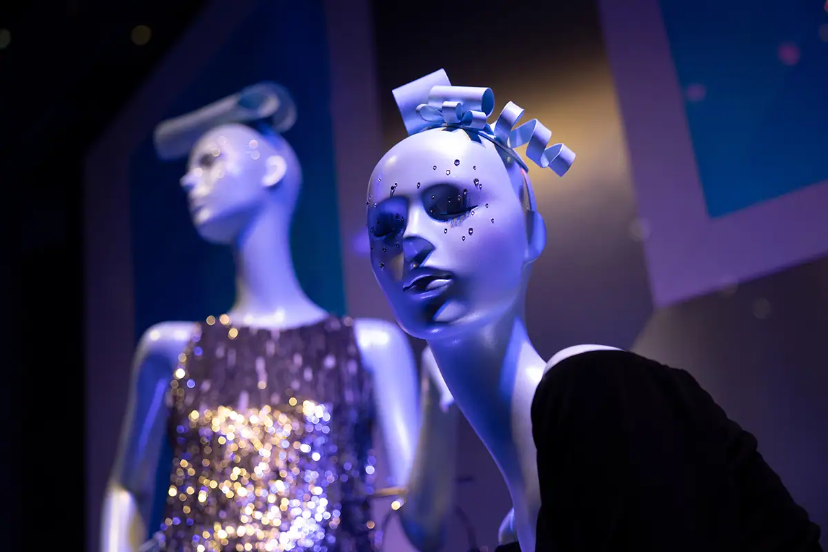 Two stylish mannequins dressed in glittering outfits under blue light, representing creative street fashion photography and urban window display art.