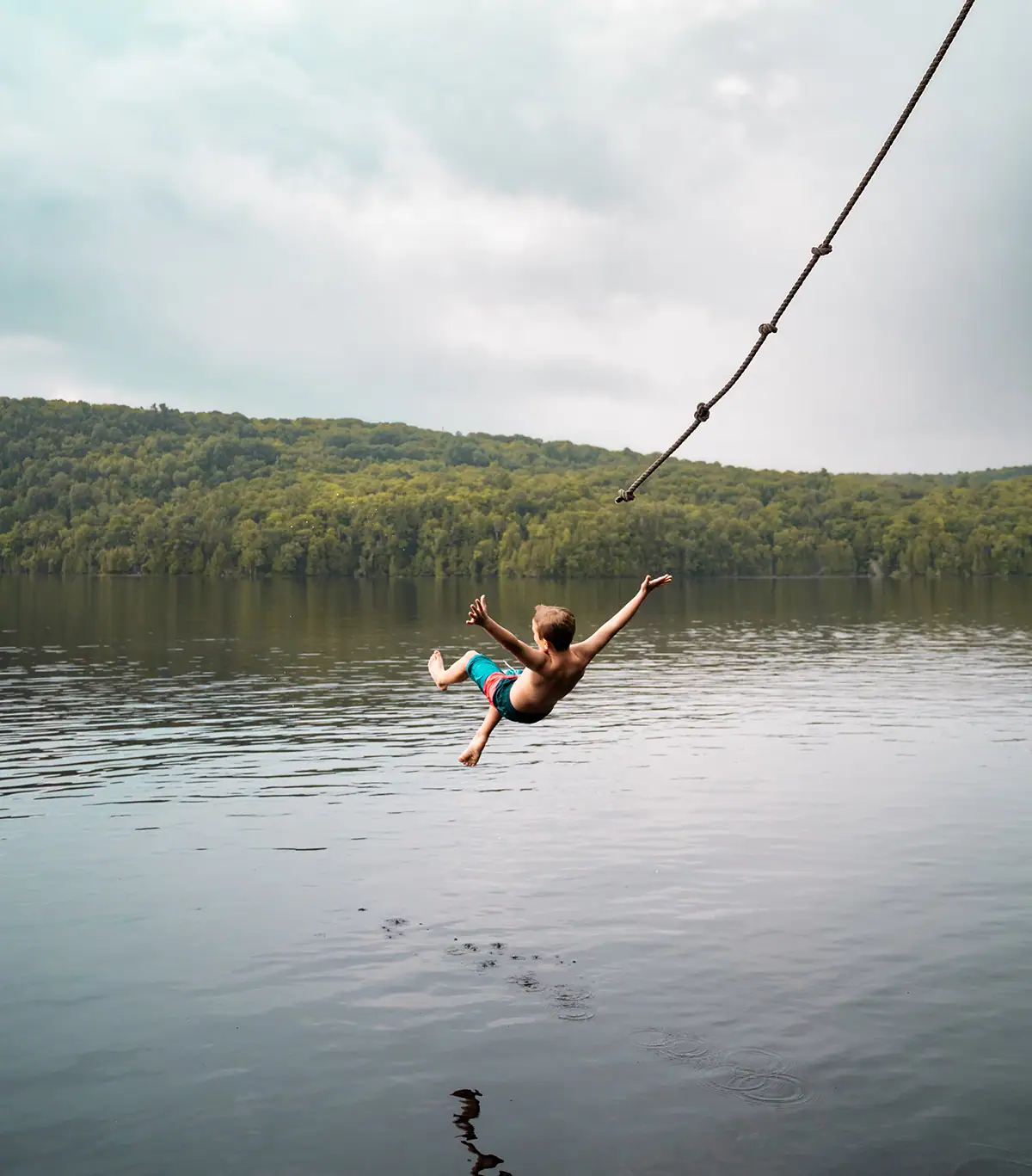 Garçon en plein vol après avoir sauté d'une balançoire à corde au-dessus d'un lac calme, photographié avec le Tamron 28-75 G2 qui met en valeur la précision du moteur autofocus.