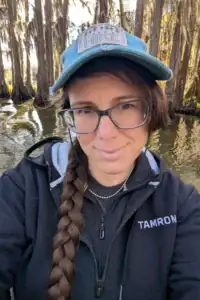 Portrait de la photographe naturaliste Alyce Bender dans un marais du sud, vêtue d'une veste Tamron alors qu'elle photographie les zones humides.