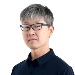 Portrait of a professional sports photographer Kazuyuki Ogawa wearing glasses against a neutral background.