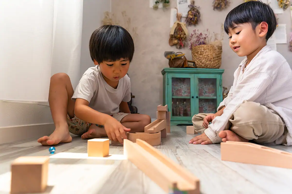 Dos niños pequeños sentados en el piso jugando con bloques de madera bajo una suave luz interior, fotografiados con el Tamron 28-75 mm F2.8 G2.