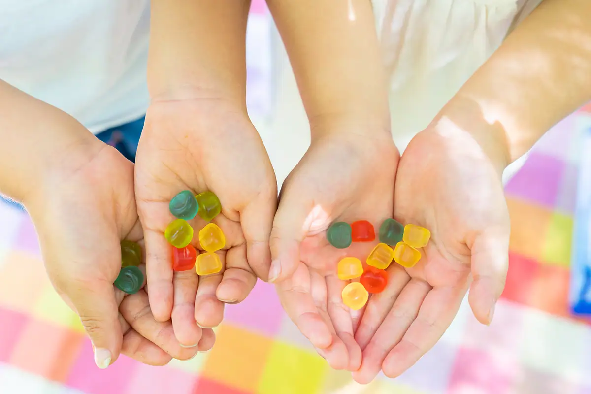 Primer plano de las manos de unos niños sosteniendo gomitas de colores al aire libre, fotografiadas con el Tamron 28-75 mm F2.8 G2 para fotografía familiar.