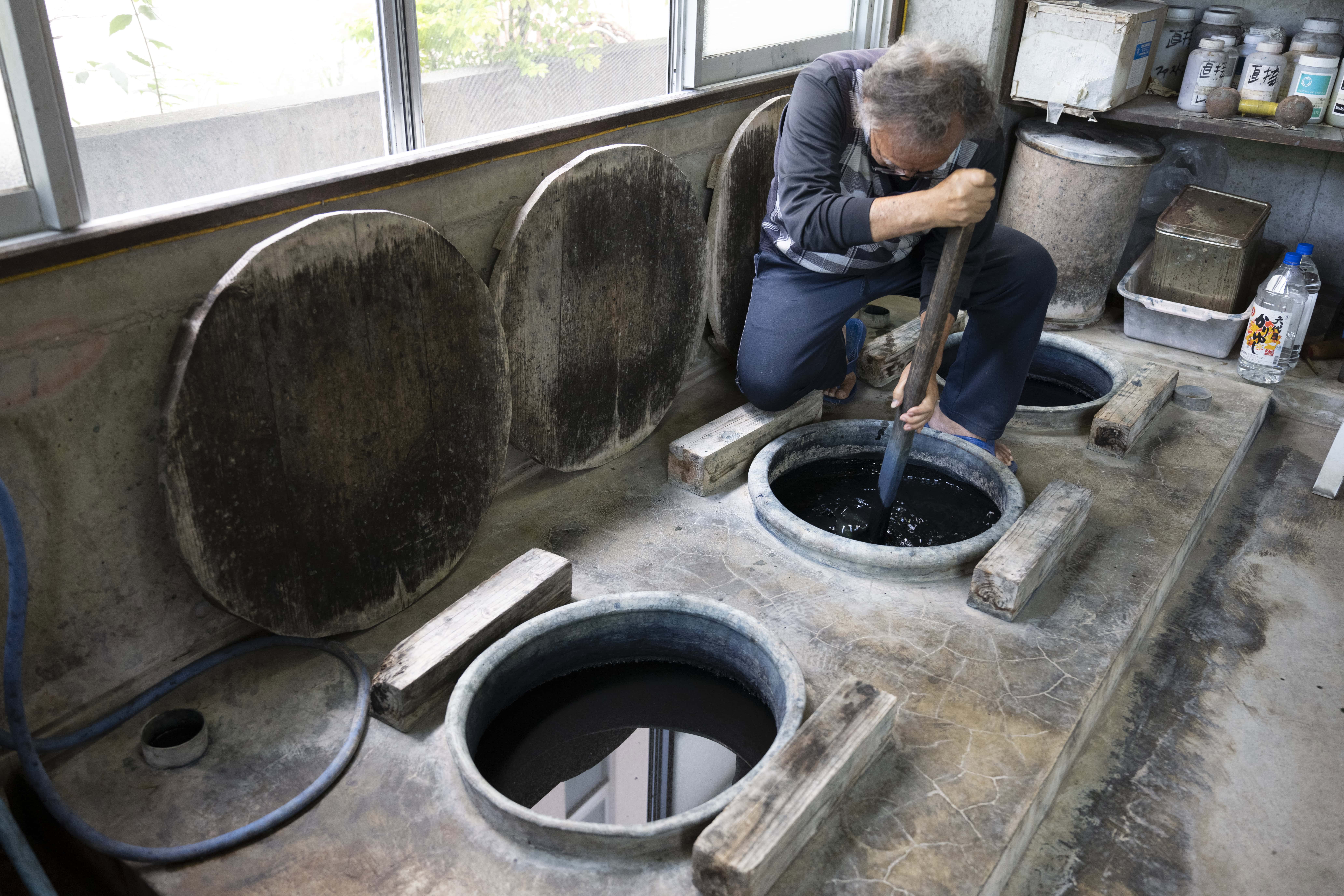 Artisan Ryukyu Kasuri remuant des cuves de teinture dans un atelier traditionnel d'Okinawa, photographié avec le Tamron 28-75mm F2.8 G2 pour un projet documentaire de narration visuelle.