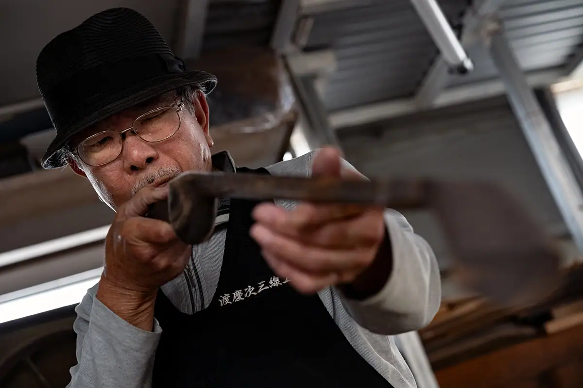Artisan SANSHIN d'Okinawa inspectant un instrument sculpté à la main, photographié avec le Tamron 28-75mm F2.8 G2 pour un documentaire de narration visuelle.