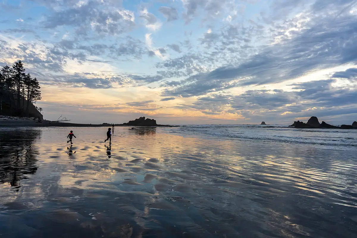 Enfants courant le long du rivage réfléchissant au coucher du soleil sur la péninsule olympique, photographiés avec le Tamron 28-75mm F2.8 G2 lors d'un voyage dans le nord-ouest du Pacifique.