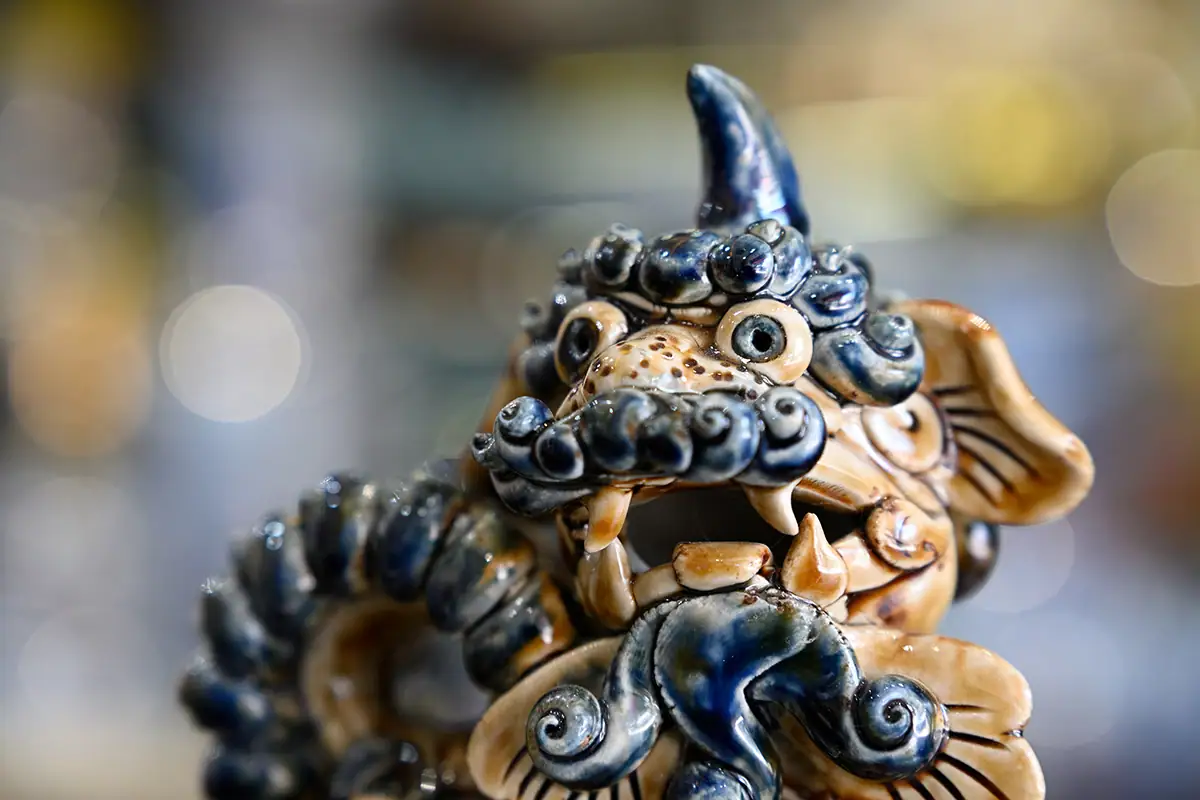 Primer plano de una figura de león de cerámica hecha a mano en el pueblo alfarero de Bát Tràng, con un suave bokeh circular detrás, fotografiada con el Tamron 28-75 mm F2.8 G2.