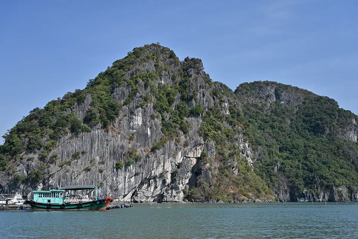 Escarpados acantilados de piedra caliza que se elevan sobre las tranquilas aguas de la bahía de Hạ Long con un barco tradicional vietnamita, fotografiado con el Tamron 28-75 mm F2.8 G2.