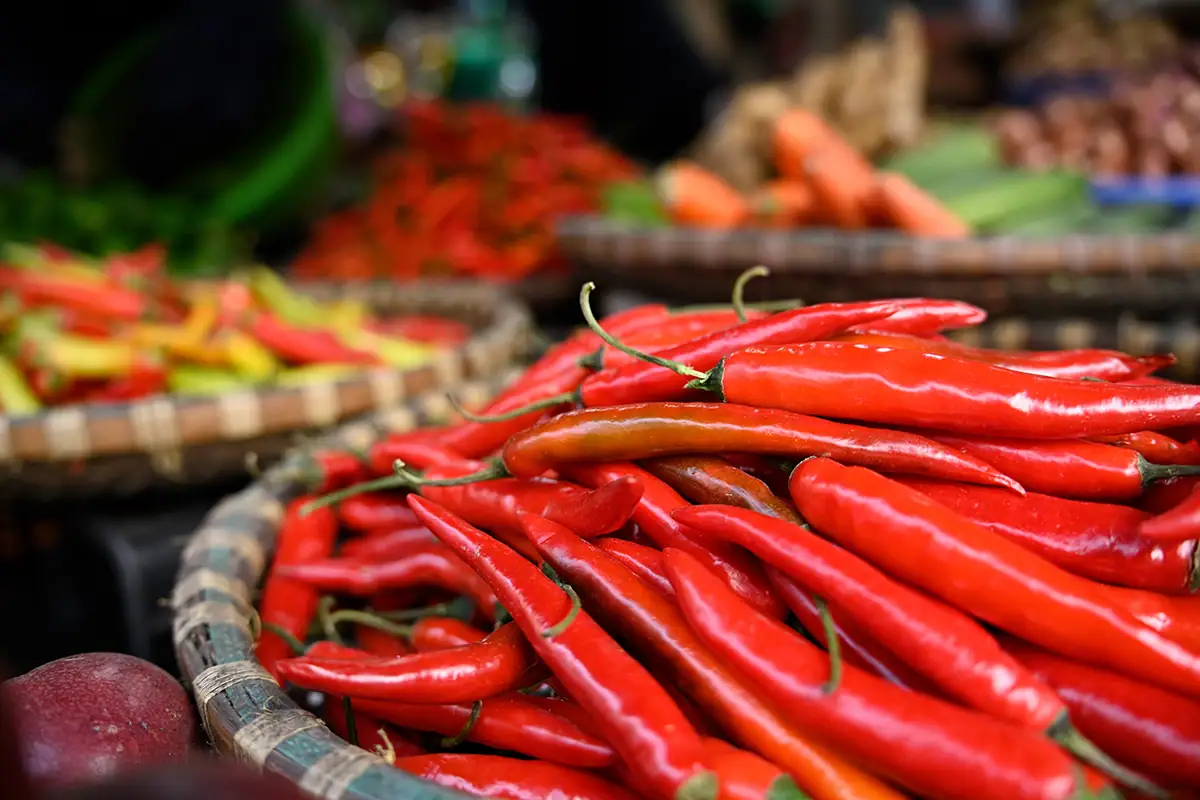Primer plano de chiles rojos brillantes en una canasta tejida en un mercado vietnamita, capturado con un suave efecto bokeh de fondo utilizando el Tamron 28-75 mm F2.8 G2.