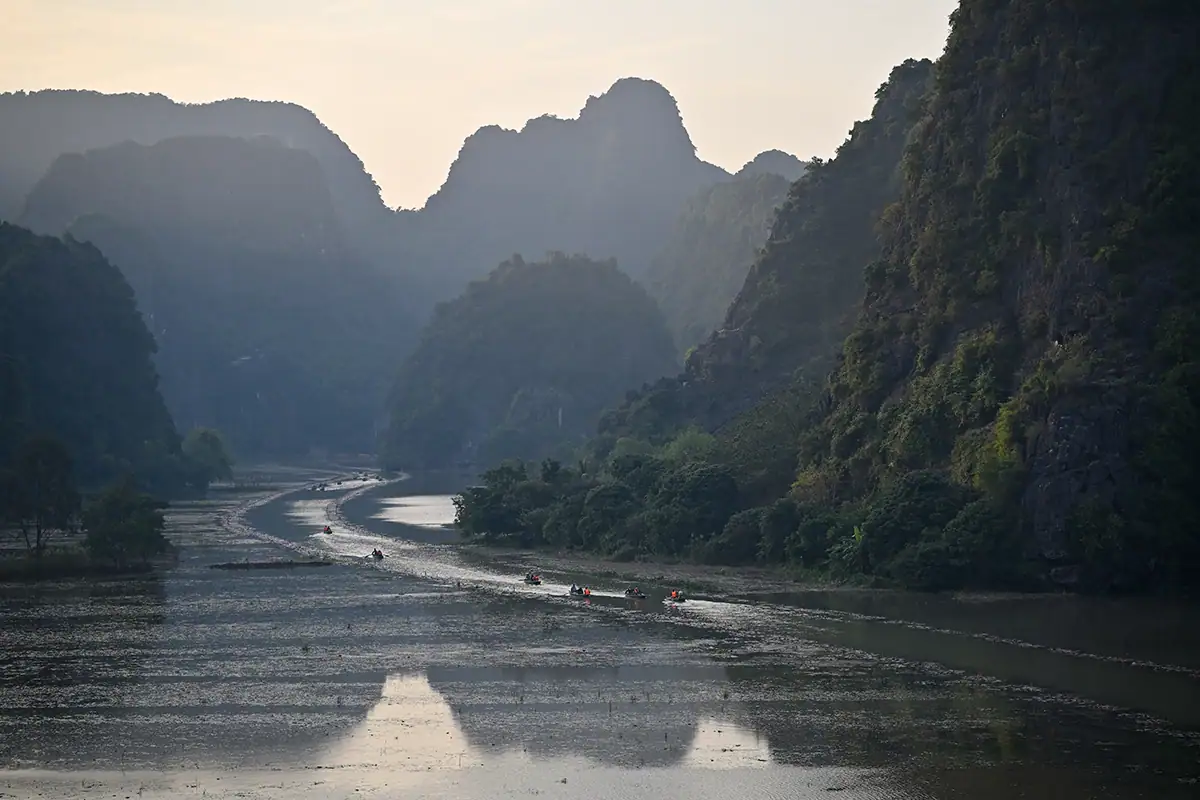 Barcos fluviales navegando por el sinuoso canal de Tam Cốc al atardecer, enmarcados por montañas de piedra caliza y una suave luz atmosférica, fotografiados con el Tamron 28-75 mm F2.8 G2.