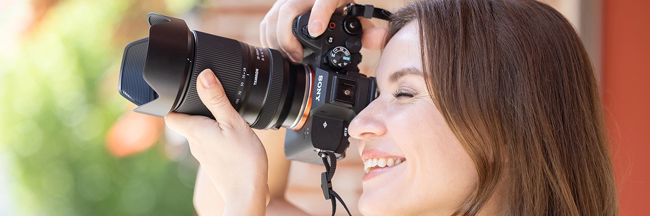 Mulher sorrindo enquanto segura uma câmera sem espelho com uma lente acoplada em uma luz externa brilhante.