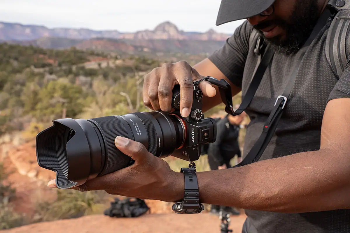 Photographer holding a Tamron camera lens with optical image stabilization during handheld shooting.