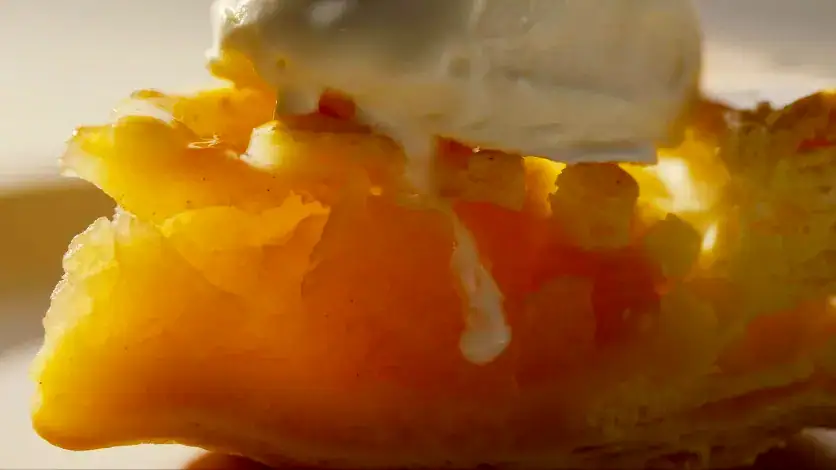 Macro gros plan de la garniture d'une tarte aux pommes avec de la crème glacée fondante pour un riche effet de grésillement et un doux bokeh cinématographique.