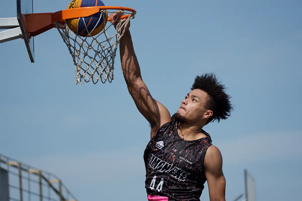 Jogador de basquete no meio de uma enterrada capturada com uma lente teleobjetiva, congelando a ação e isolando o atleta.