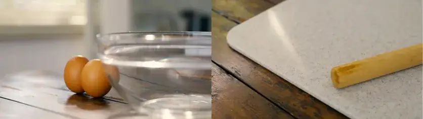 Eggs and a glass bowl on a wooden table beside a cutting board and rolling pin.