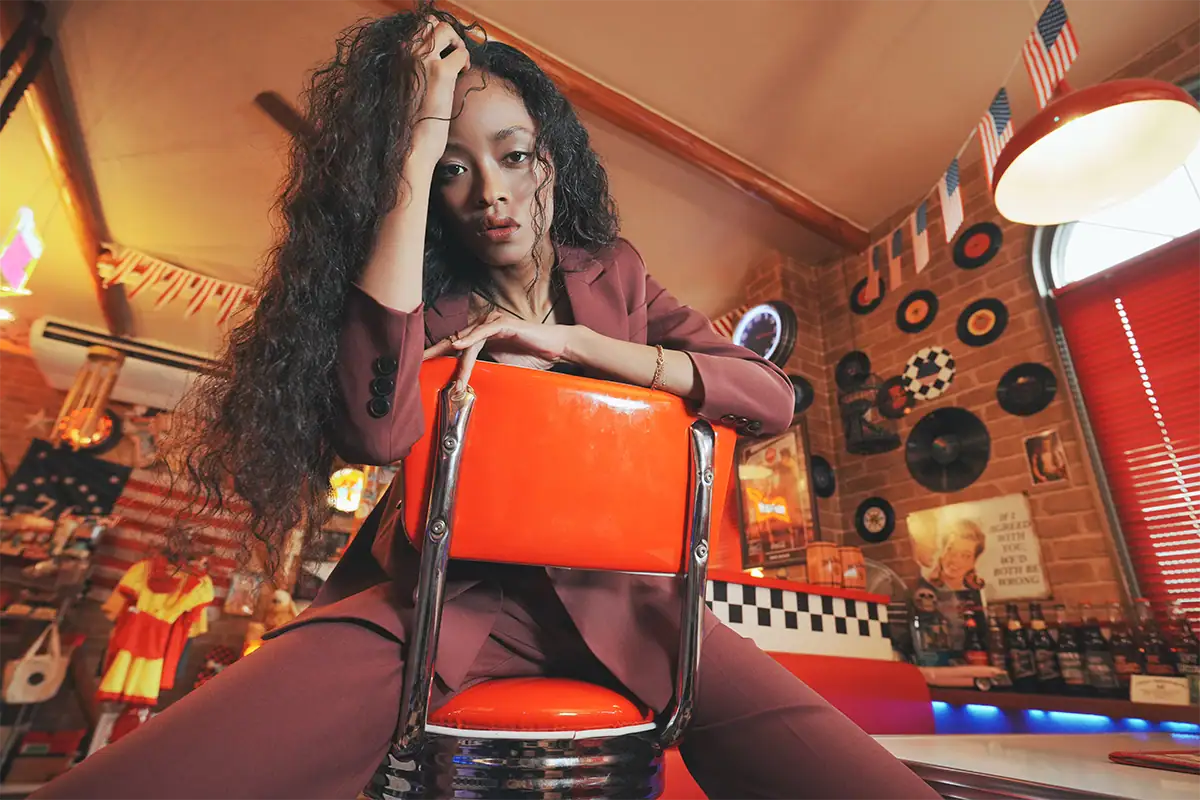 Retrato ambiental de una mujer posando en interiores sobre una silla roja en un restaurante de estilo retro, fotografiada con una perspectiva gran angular.